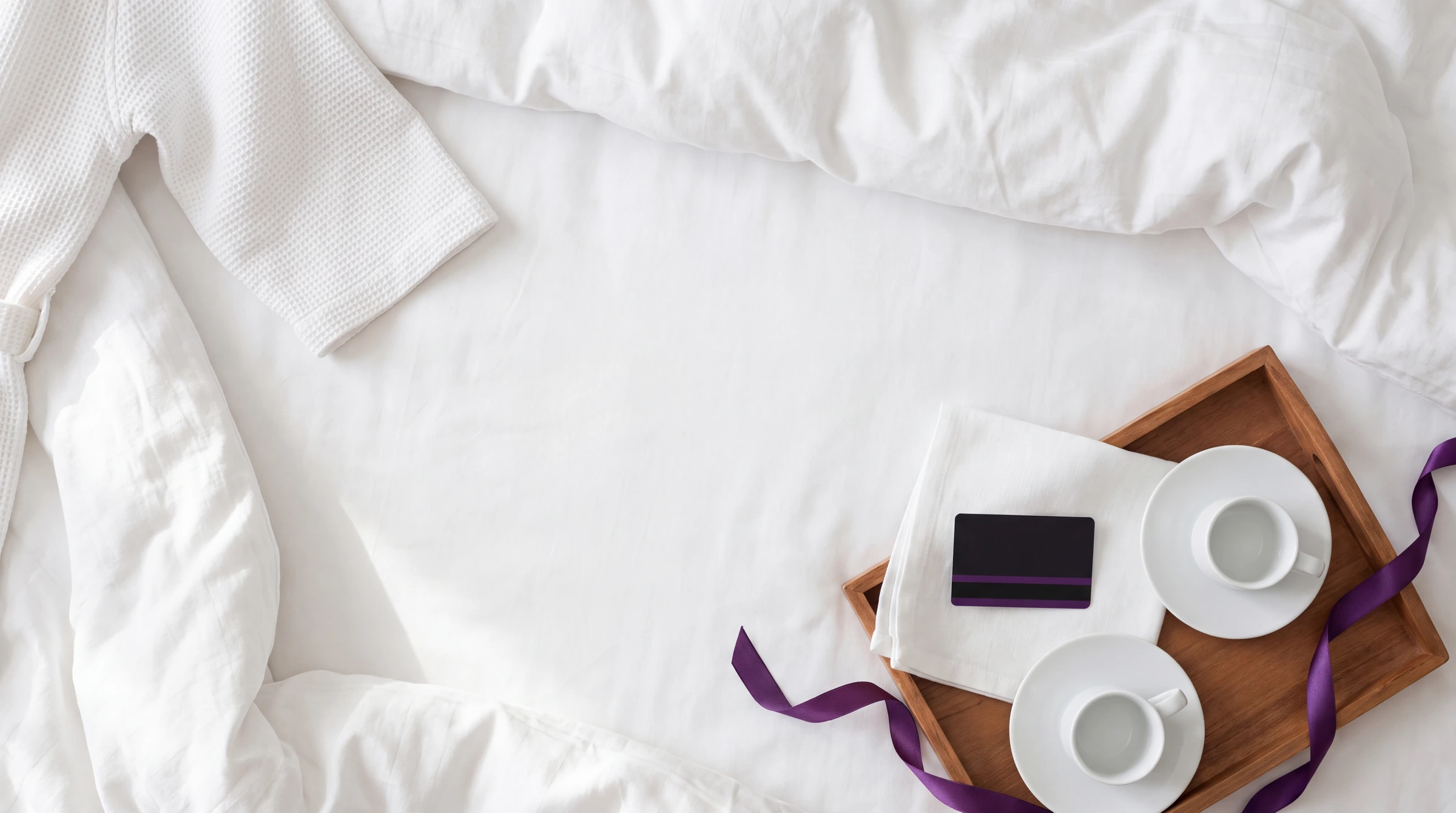 A breakfast tray and a purple ribbon on a white hotel bed